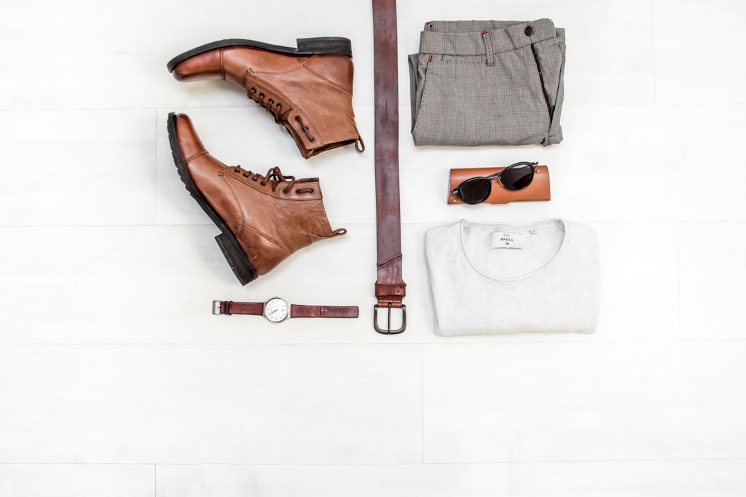 capsule wardrobe essentials flat lay with neutral-toned blazer, shirts, jeans, knitwear, belt, and leather accessories neatly arranged